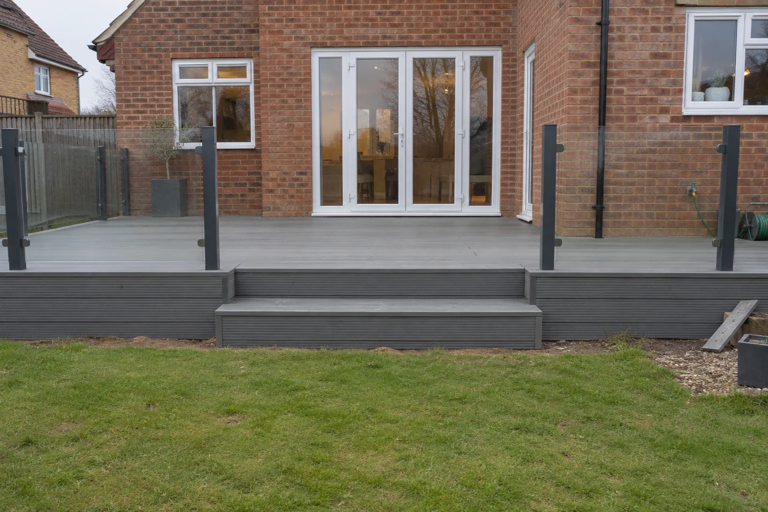 Composite decking with a glass balustrade and steps leading down to a lawn.
