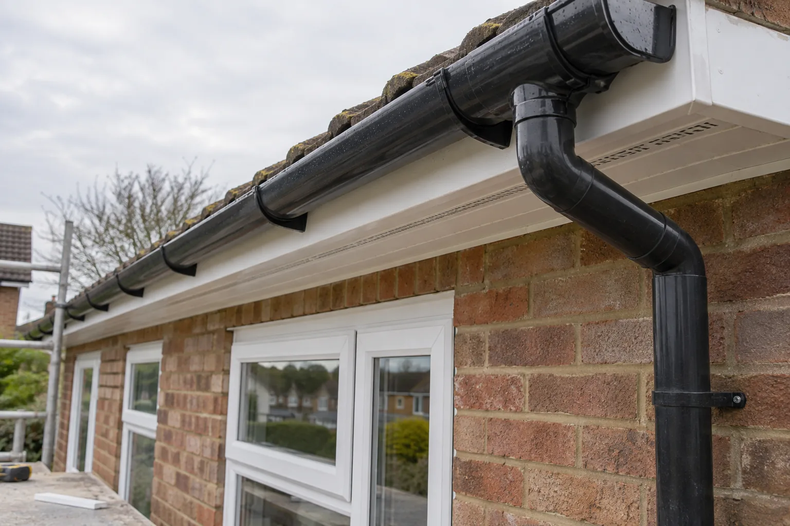 White fascias and ventilated soffits with black guttering and a downpipe on a brick bungalow.